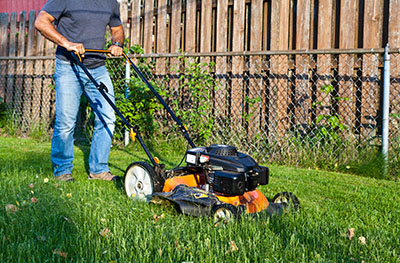 Man,In,Blue,Jeans,Mowing,Lawn,On,His,Backyard.